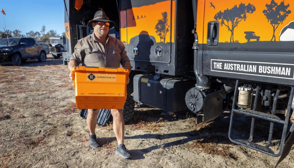 man carrying a camping storage box by campervan